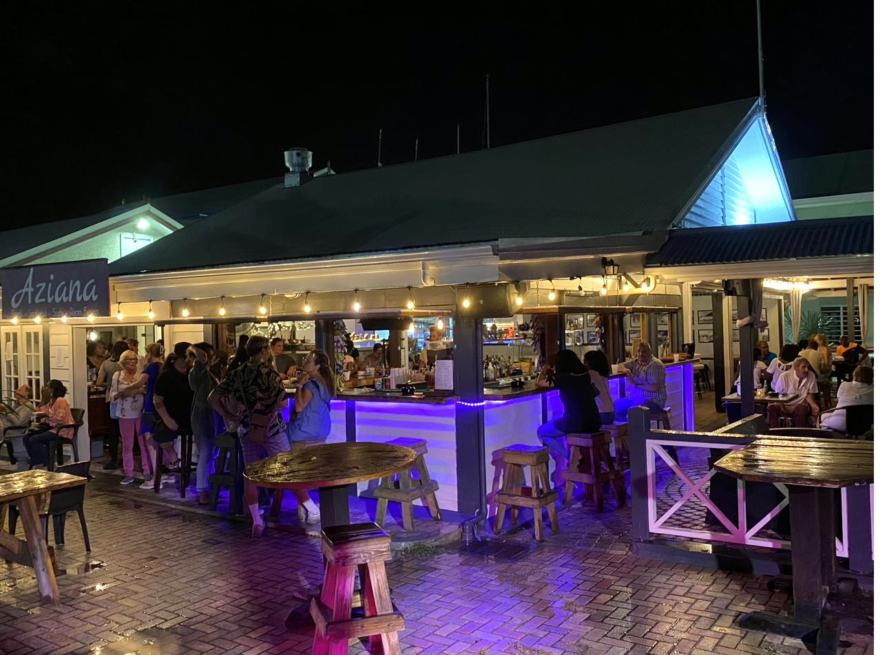 Aziana at night — the bar lit with purple LED glow, the Aziana sign visible, marina village setting